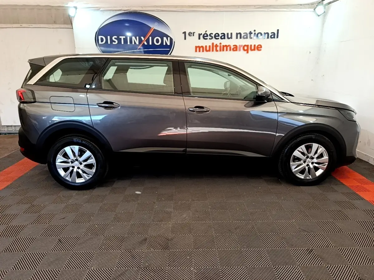 Profil droit d’un Peugeot 5008 gris clair 2021 garé en intérieur avec jantes alliage et rétroviseurs noirs.