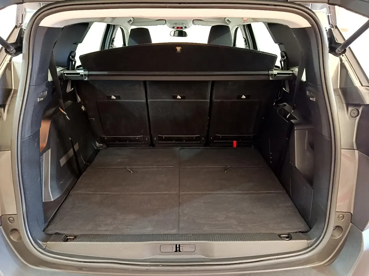 Coffre ouvert vu de l'arrière d'un Peugeot 5008 gris clair, banquette arrière rabattue et cache-bagages en place.