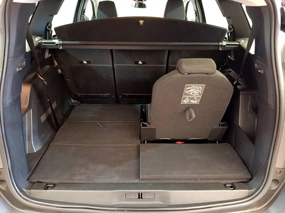 Vue arrière du coffre ouvert du Peugeot 5008 gris clair, montrant la troisième rangée de sièges partiellement rabattue.