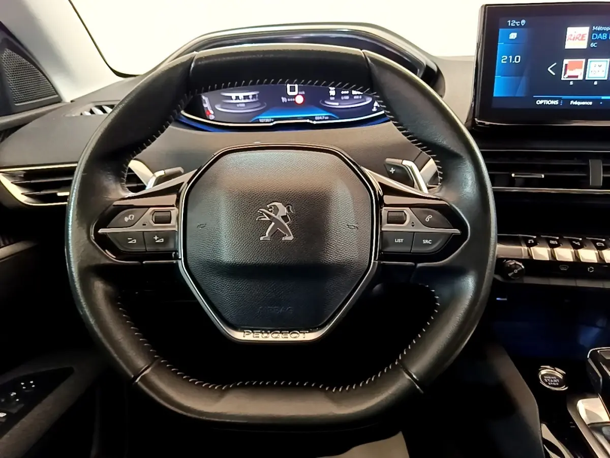 Vue intérieure centrée sur le volant cuir noir du Peugeot 5008 2021 avec tableau de bord numérique et écran tactile.