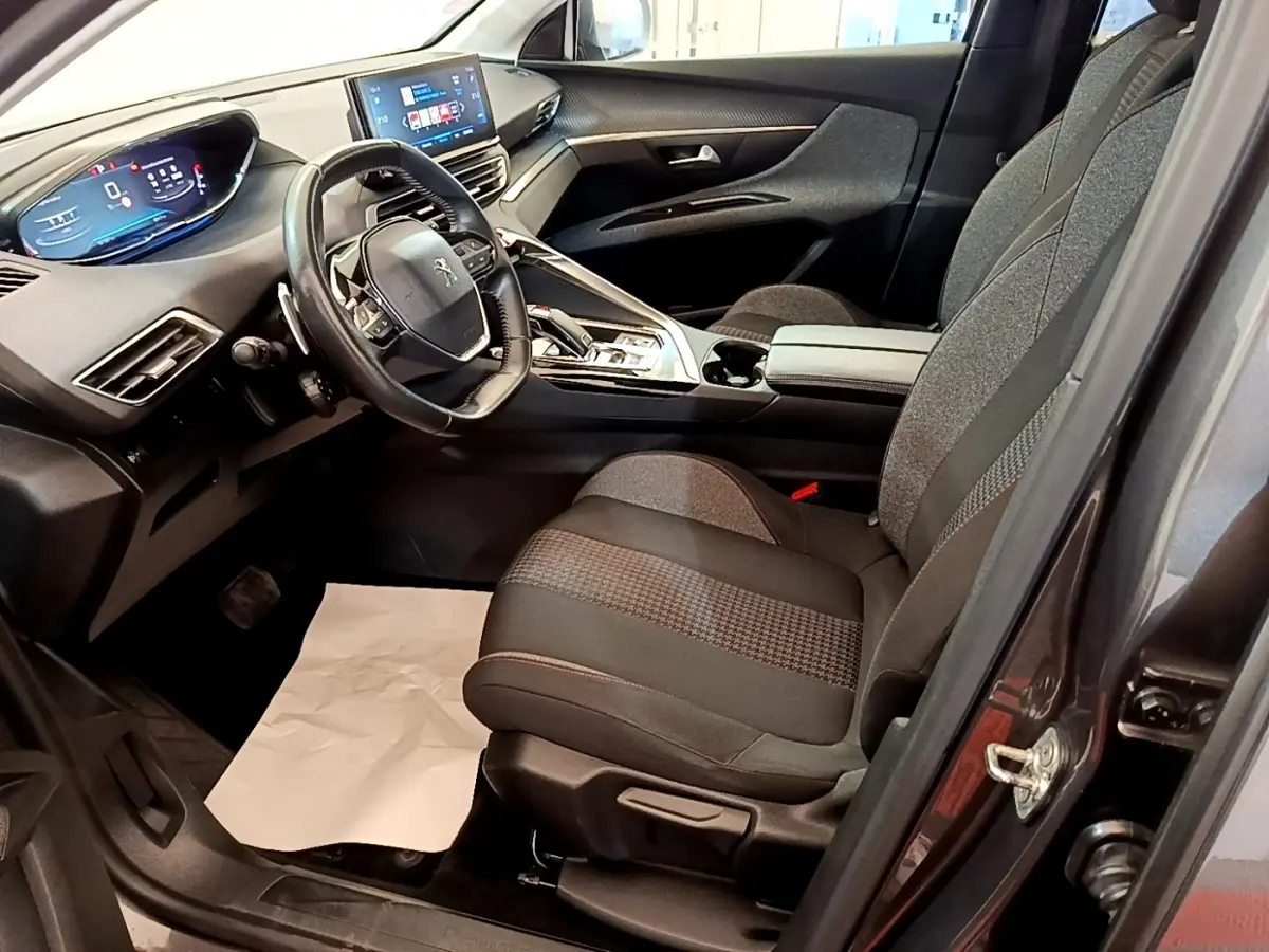 Vue intérieure côté conducteur du Peugeot 5008 gris clair, mettant en valeur le volant cuir et l'écran tactile central.
