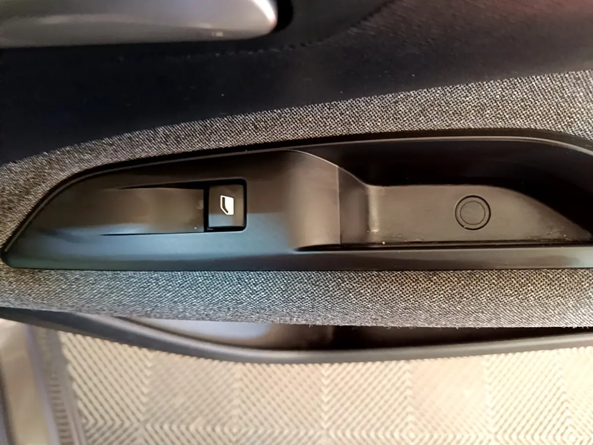 Gros plan sur la poignée intérieure de porte avec bouton de verrouillage, tissu gris clair visible autour.