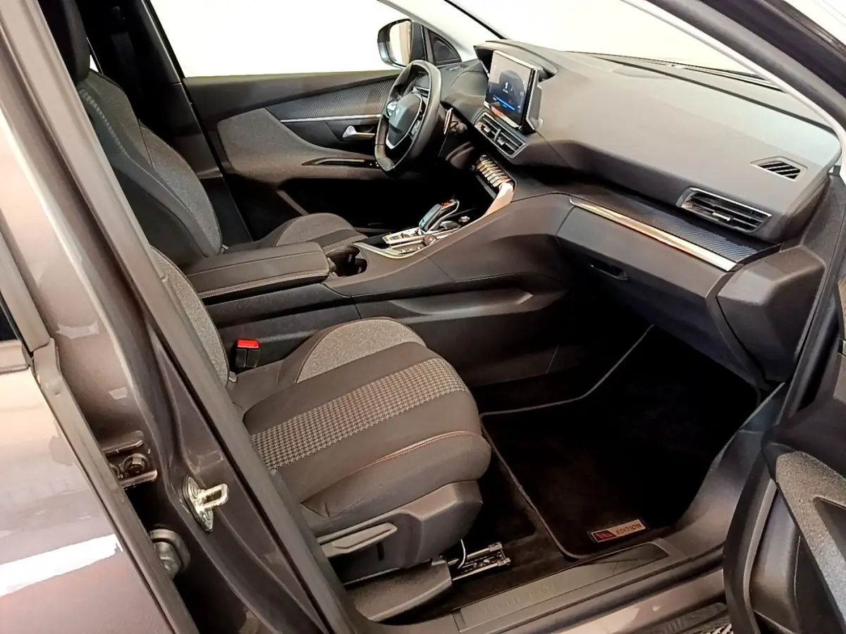 Vue intérieure côté conducteur du Peugeot 5008 gris clair, mettant en valeur le tableau de bord et l’écran tactile central.