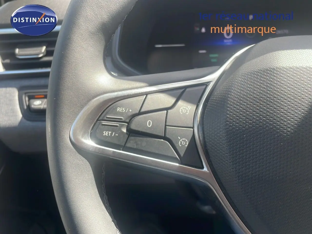 Gros plan sur les commandes au volant à gauche d’une Renault Clio blanche 2025, avec boutons de régulateur de vitesse.