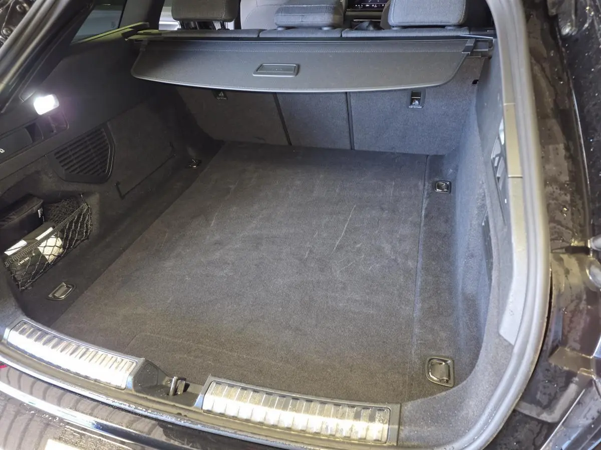 Coffre ouvert vu de l'arrière d'une Audi A5 Avant noir avec tapis de sol et cache-bagages déployé.