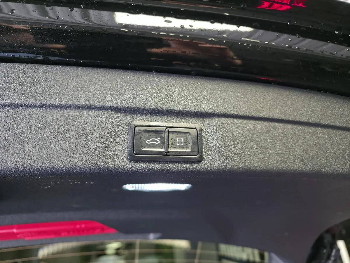 Gros plan sur les boutons d'ouverture et de verrouillage du hayon d'une Audi A5 Avant noire, vue intérieure du coffre.