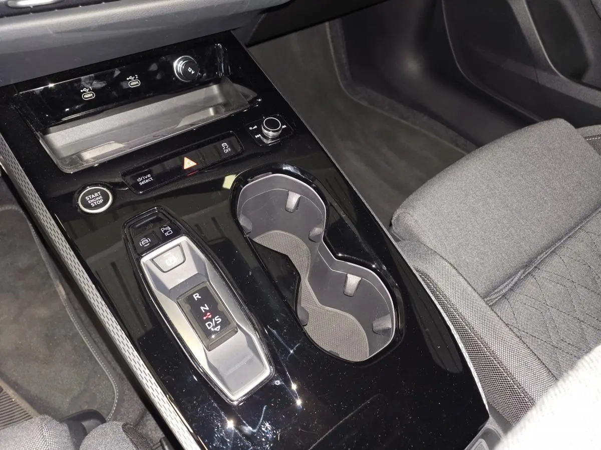 Vue rapprochée de la console centrale noire brillante de l'Audi A5 Avant 2025 avec levier de vitesse automatique et porte-gobelets.