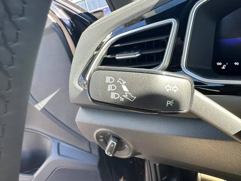 Gros plan sur la commande des phares à gauche du volant dans l’habitacle noir du Volkswagen T-Roc 2025.