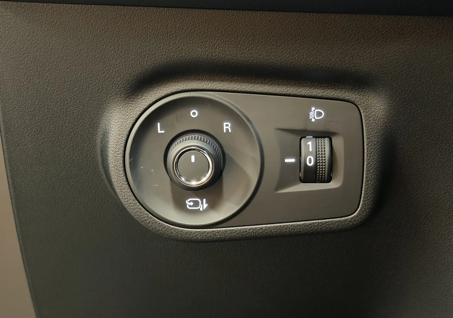 Gros plan sur les commandes de réglage des rétroviseurs et de l’éclairage du MG ZS noir, intérieur côté conducteur.