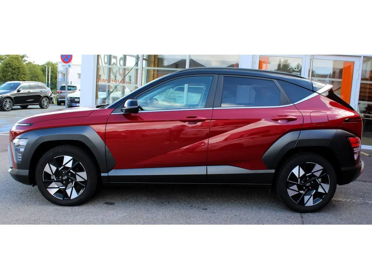 Vue latérale droite du Hyundai Kona 2024 rouge Ultimate Metal avec toit noir et protections d'ailes anthracite.