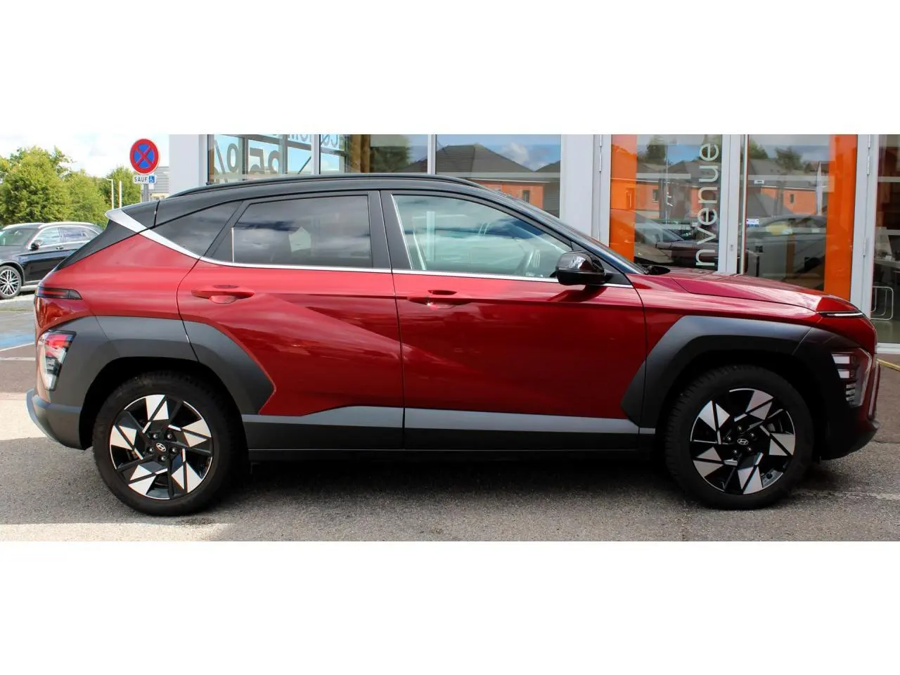 Hyundai Kona 2024 rouge Ultimate Metal avec toit noir, vue profil côté gauche, jantes alliage et protections noires.