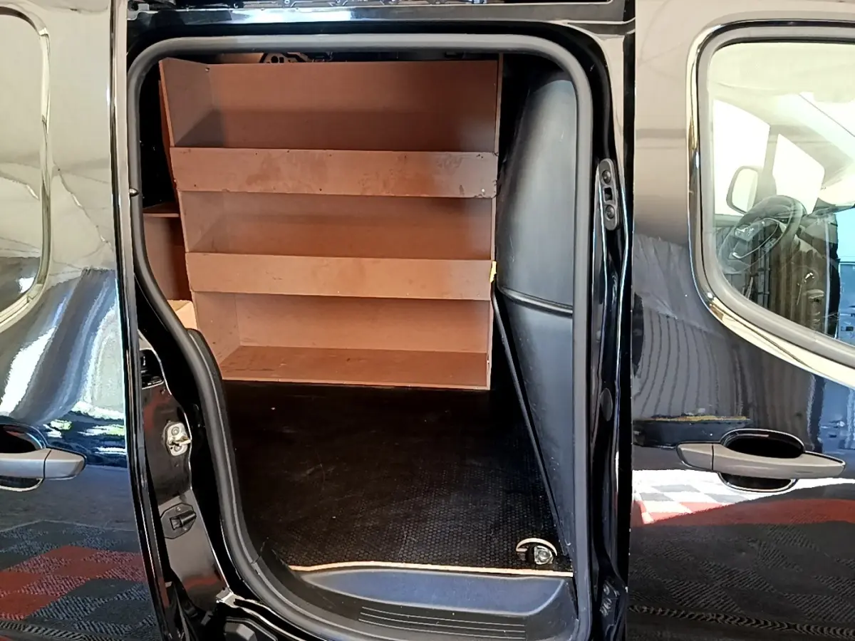 Vue latérale du Peugeot Partner noir 2022 avec porte coulissante ouverte montrant l'aménagement intérieur avec étagères en bois.
