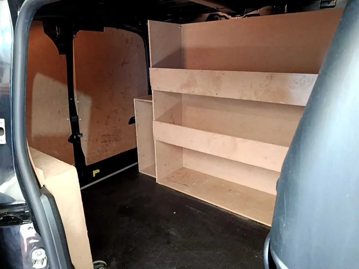 Vue intérieure arrière du Peugeot Partner noir 2022, montrant l'aménagement bois de rangement et la cloison pleine.