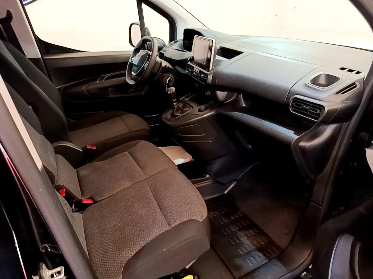 Vue intérieure côté conducteur du Peugeot Partner 2022 noir, montrant le tableau de bord et les sièges avant en tissu.