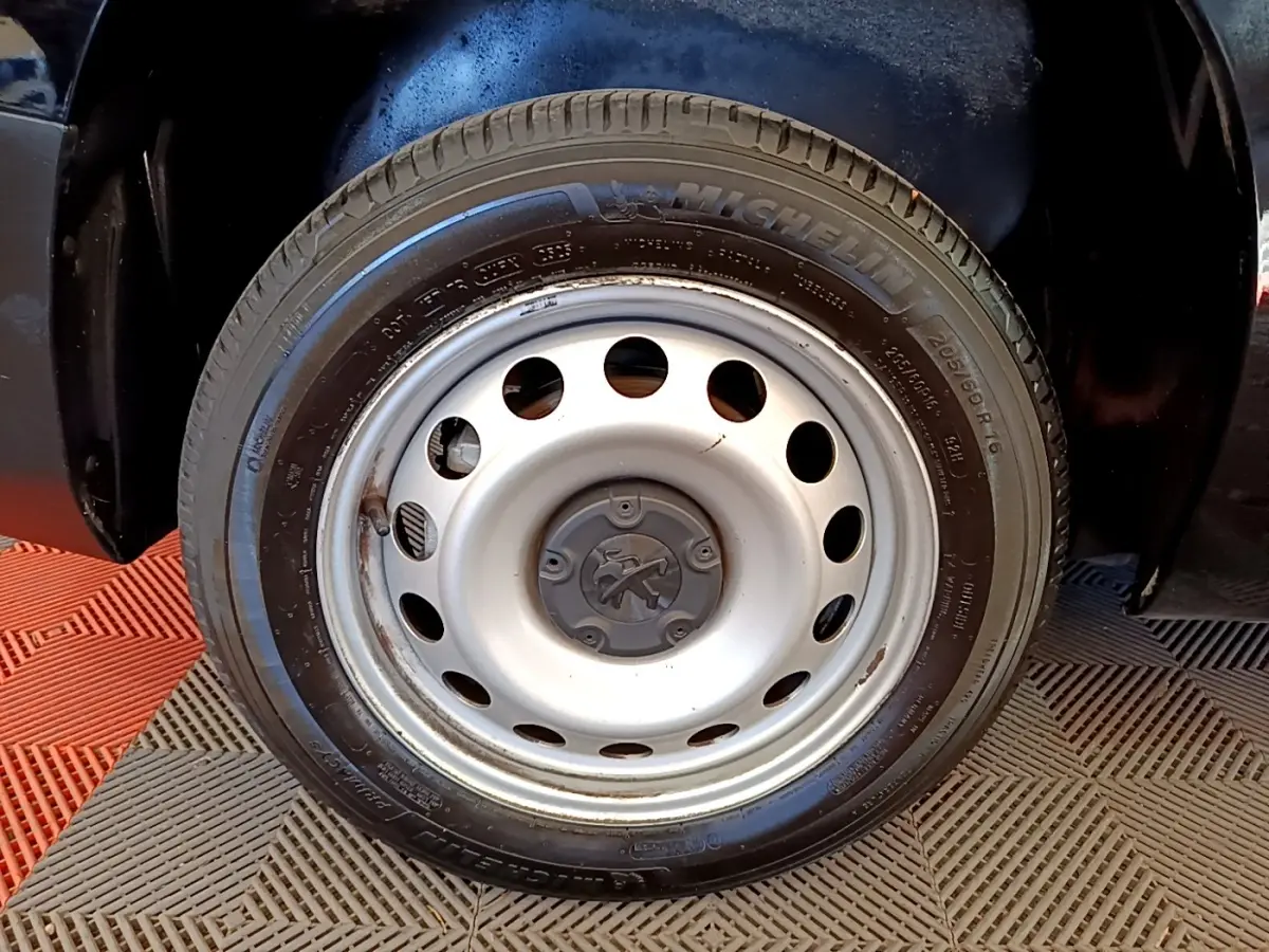 Gros plan sur la roue avant droite en jante acier argentée du Peugeot Partner noir, pneu Michelin visible.