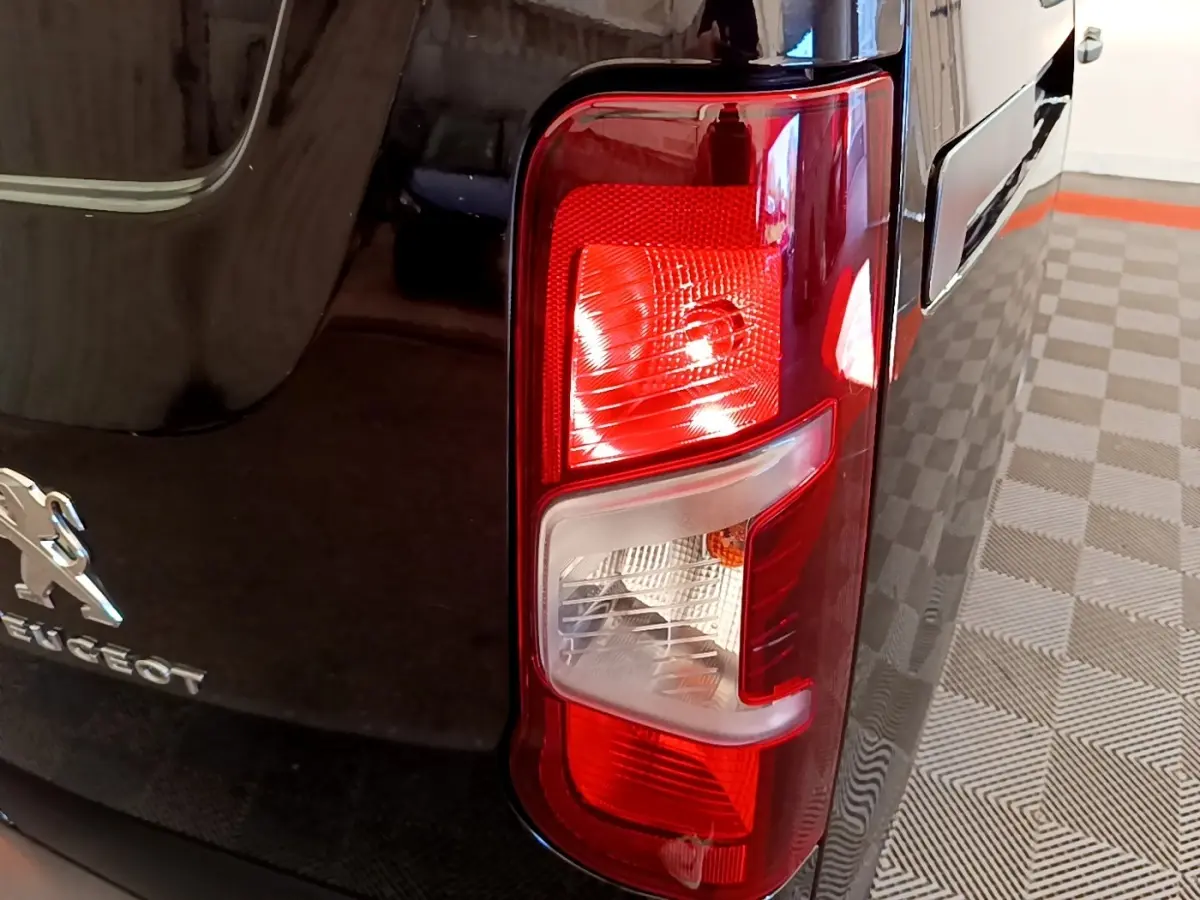 Gros plan sur le feu arrière droit rouge et blanc d’un Peugeot Partner noir, avec logo visible sur la carrosserie.