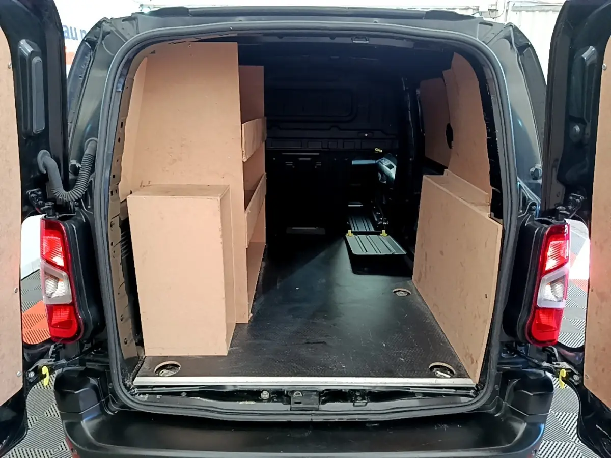 Vue arrière ouverte du Peugeot Partner noir 2022, montrant l'espace de chargement avec cloison et étagères en bois.