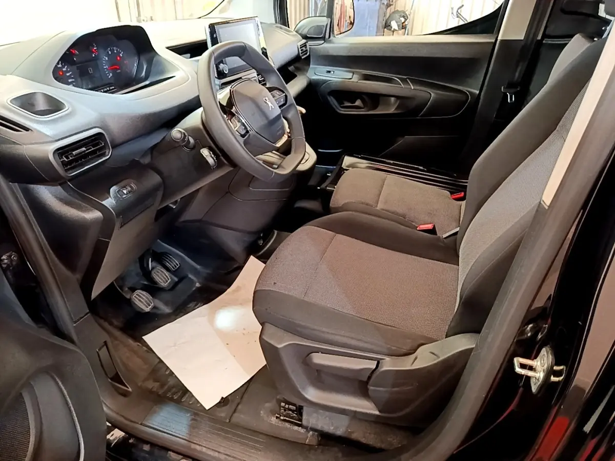 Vue intérieure côté conducteur du Peugeot Partner noir 2022, montrant le volant, tableau de bord et sièges avant.