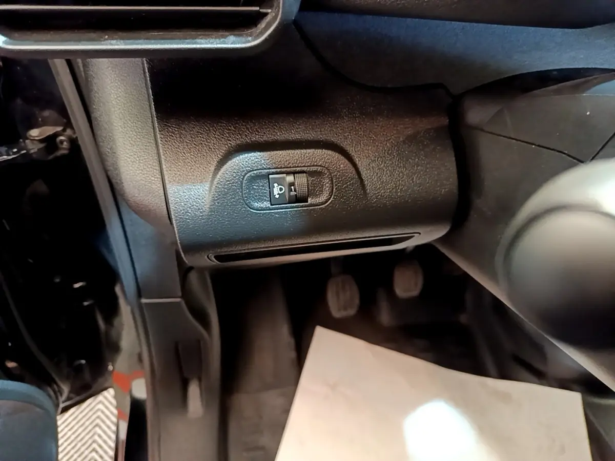 Détail intérieur côté conducteur du Peugeot Partner noir 2022, montrant le réglage manuel des phares et les pédales.