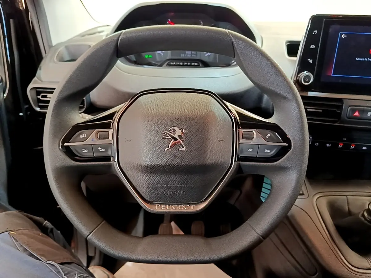 Vue rapprochée du volant noir Peugeot Partner 2022 avec commandes intégrées et tableau de bord numérique.
