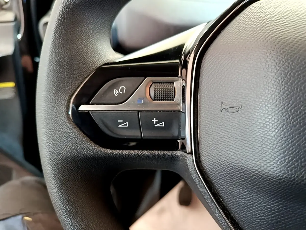 Gros plan sur les commandes gauche du volant noir du Peugeot Partner 2022, avec boutons de volume et appel mains libres.