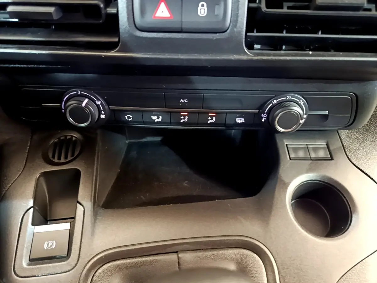 Vue rapprochée de la console centrale noire du Peugeot Partner 2022, montrant les commandes de climatisation et frein à main électrique.