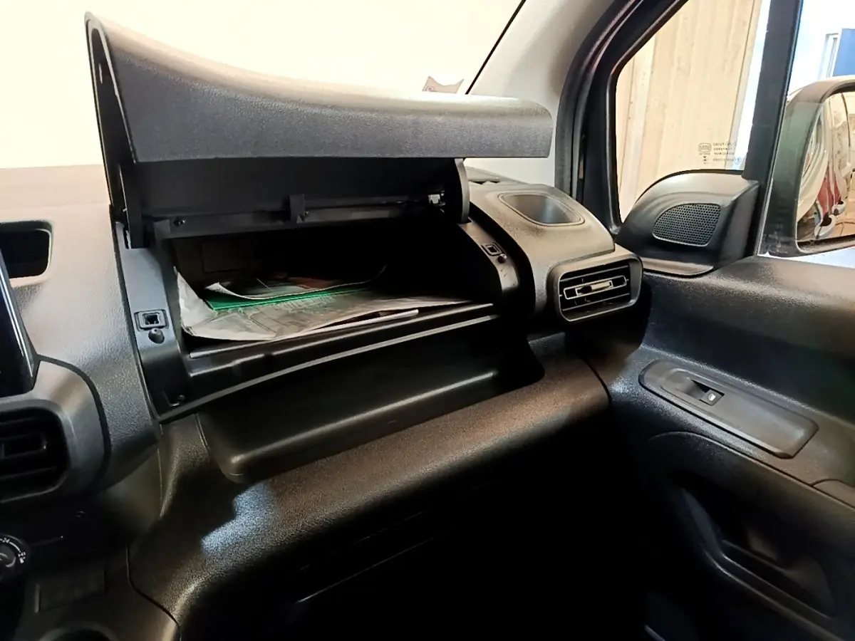 Vue intérieure du compartiment à gants ouvert côté passager du Peugeot Partner noir, montrant la console et la ventilation.