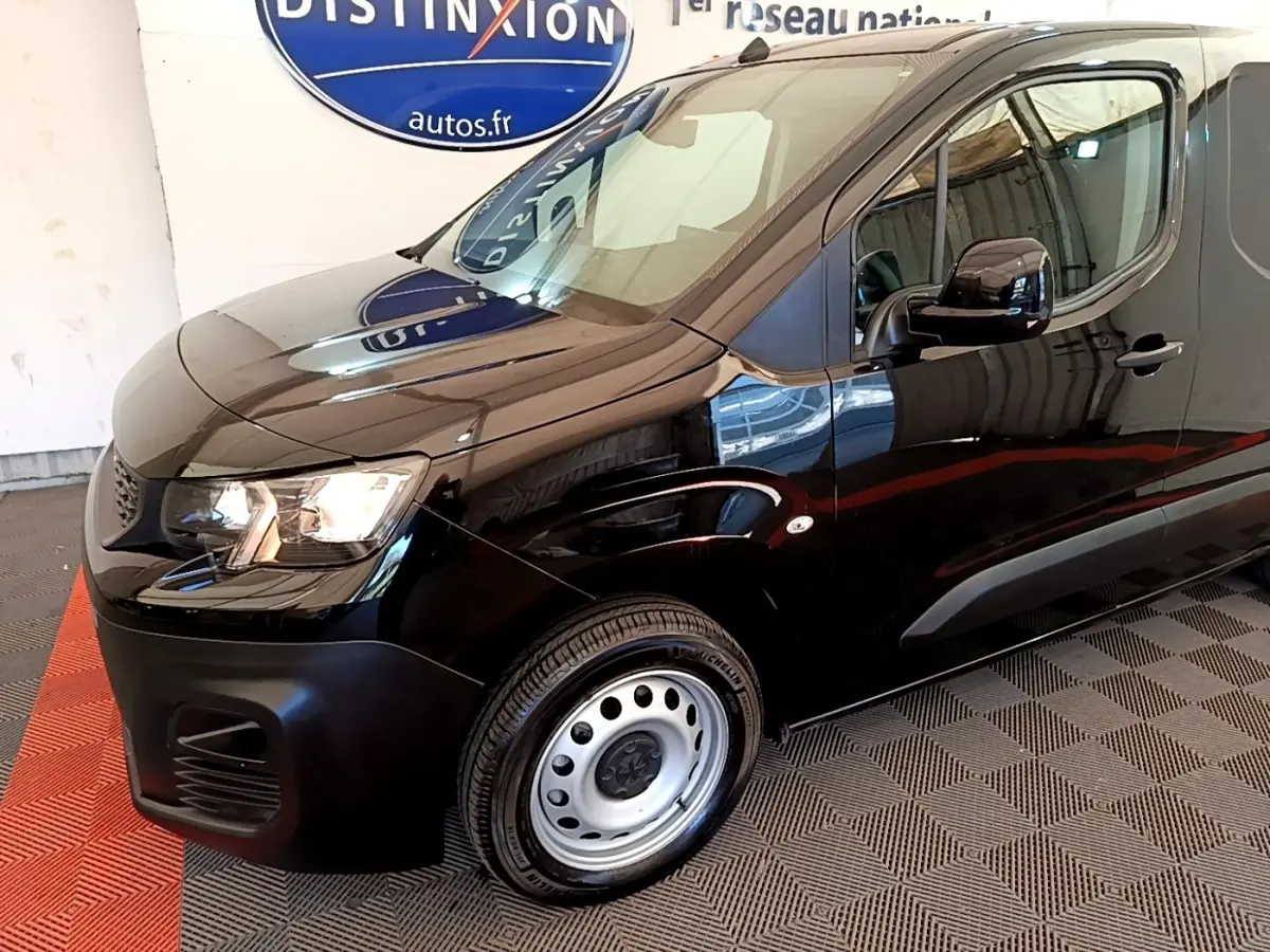 Vue 3/4 avant droit du Peugeot Partner noir avec jante acier et phares allumés en intérieur showroom.