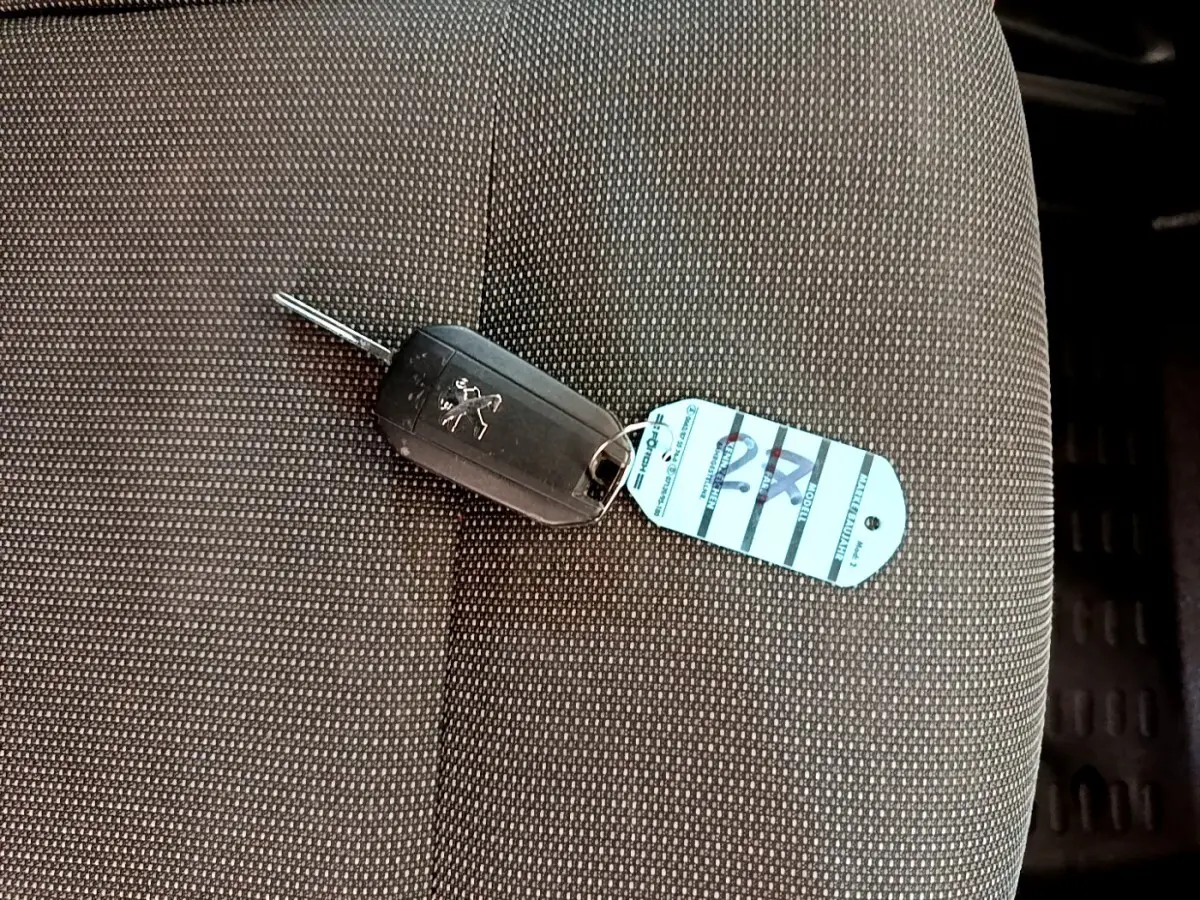 Clé de voiture Peugeot posée sur un siège tissu gris foncé à motifs fins à l'intérieur du véhicule.