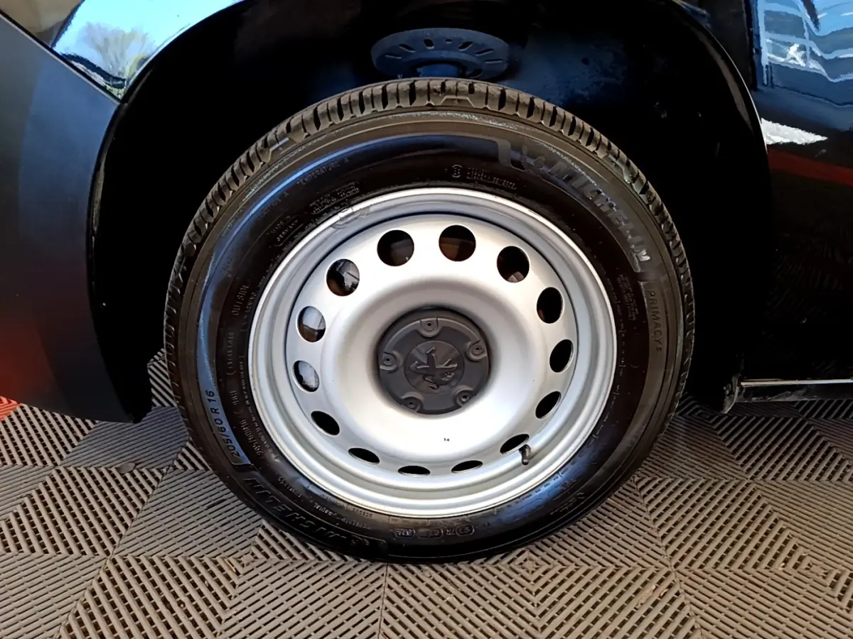 Gros plan sur la roue avant droite en jante acier argentée du Peugeot Partner noir, avec logo Peugeot au centre.