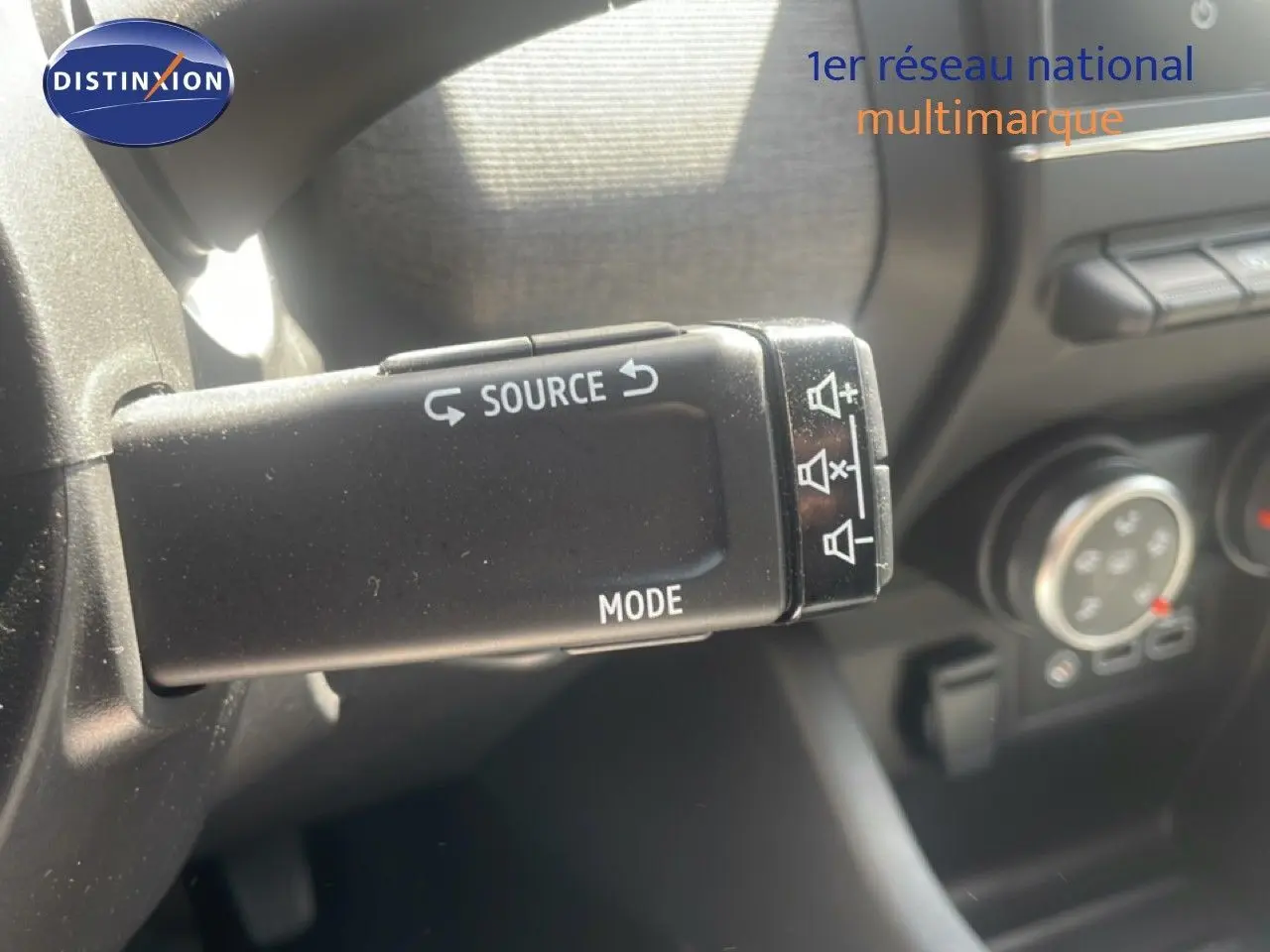 Gros plan sur la commande au volant de la Renault Clio 2025, bouton source et mode en noir mat.