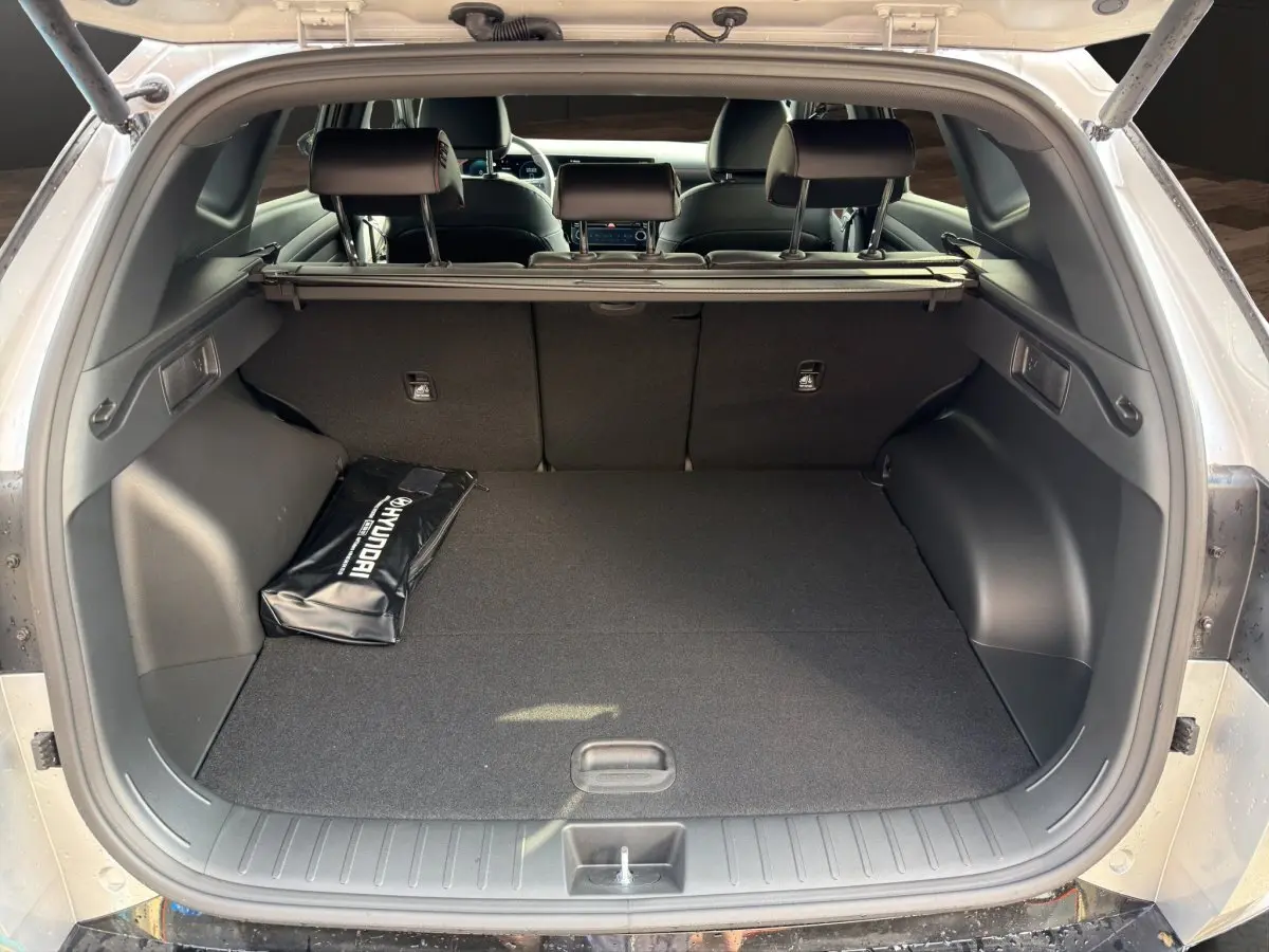 Vue arrière du coffre ouvert d’un Hyundai Tucson gris clair, avec housse d’accessoires Hyundai posée à gauche.
