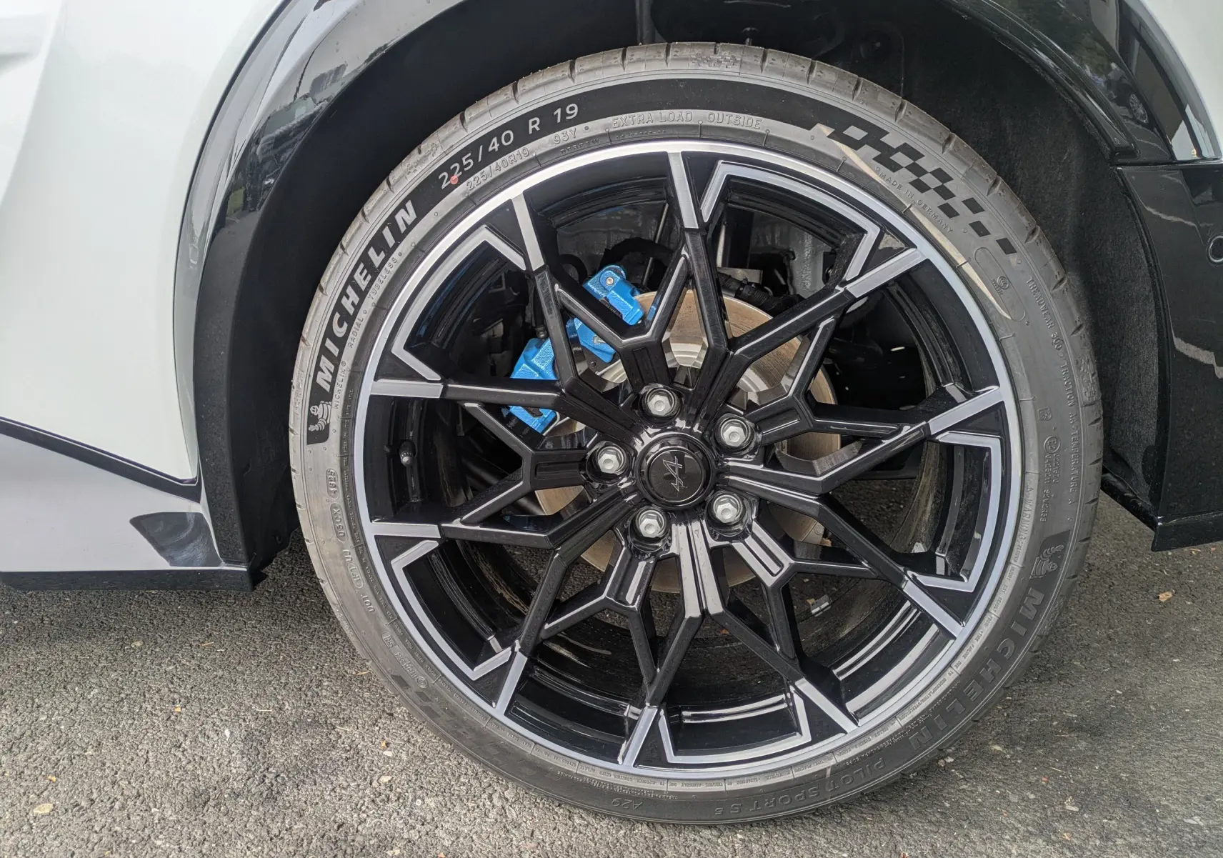 Gros plan sur la jante alliage 19'' Snowflake noir brillant et étrier de frein bleu Alpine d'une Alpine A290 blanche toit noir.
