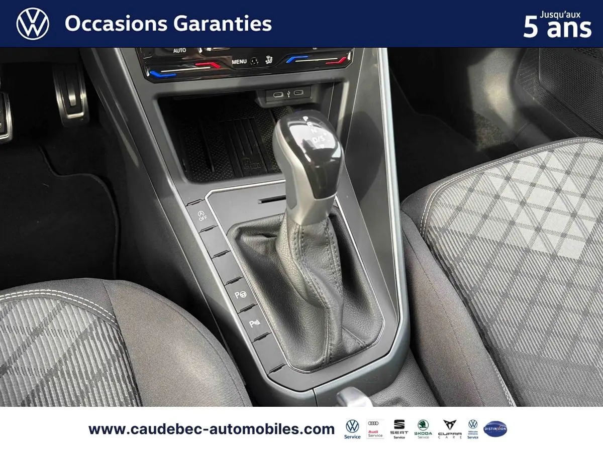 Gros plan sur la console centrale et levier de vitesse manuel d’une Volkswagen Polo rouge, sièges à motifs gris visibles.