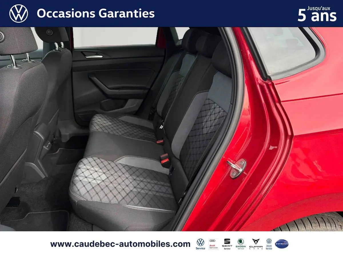 Vue côté droit arrière sur l'intérieur de la Volkswagen Polo rouge, montrant les sièges arrière en tissu gris à motifs.