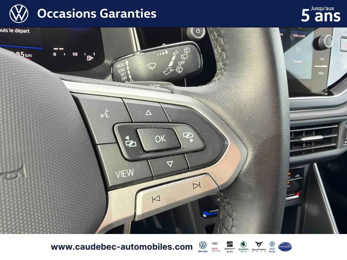 Gros plan sur les commandes multifonctions du volant cuir noir du Volkswagen Polo rouge, avec tableau de bord digital en arrière-plan.