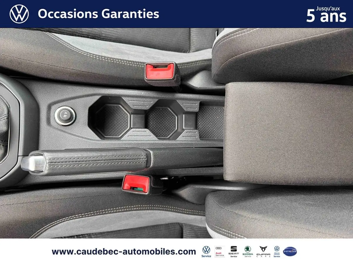 Vue plongeante sur la console centrale noire avec frein à main et deux ceintures rouges dans l'habitacle d'une Volkswagen Polo.