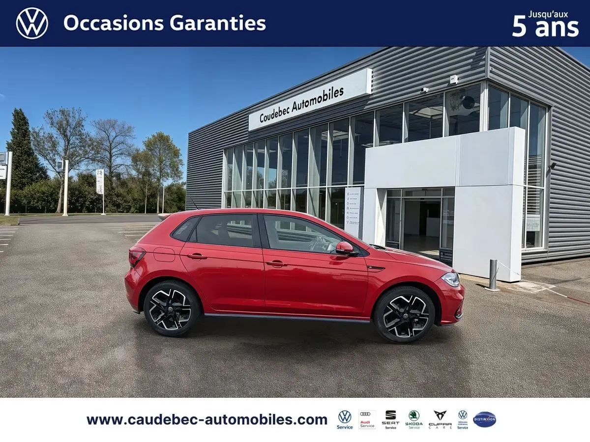 Profil droit d'une Volkswagen Polo rouge 2025 garée devant un bâtiment moderne de concession automobile.