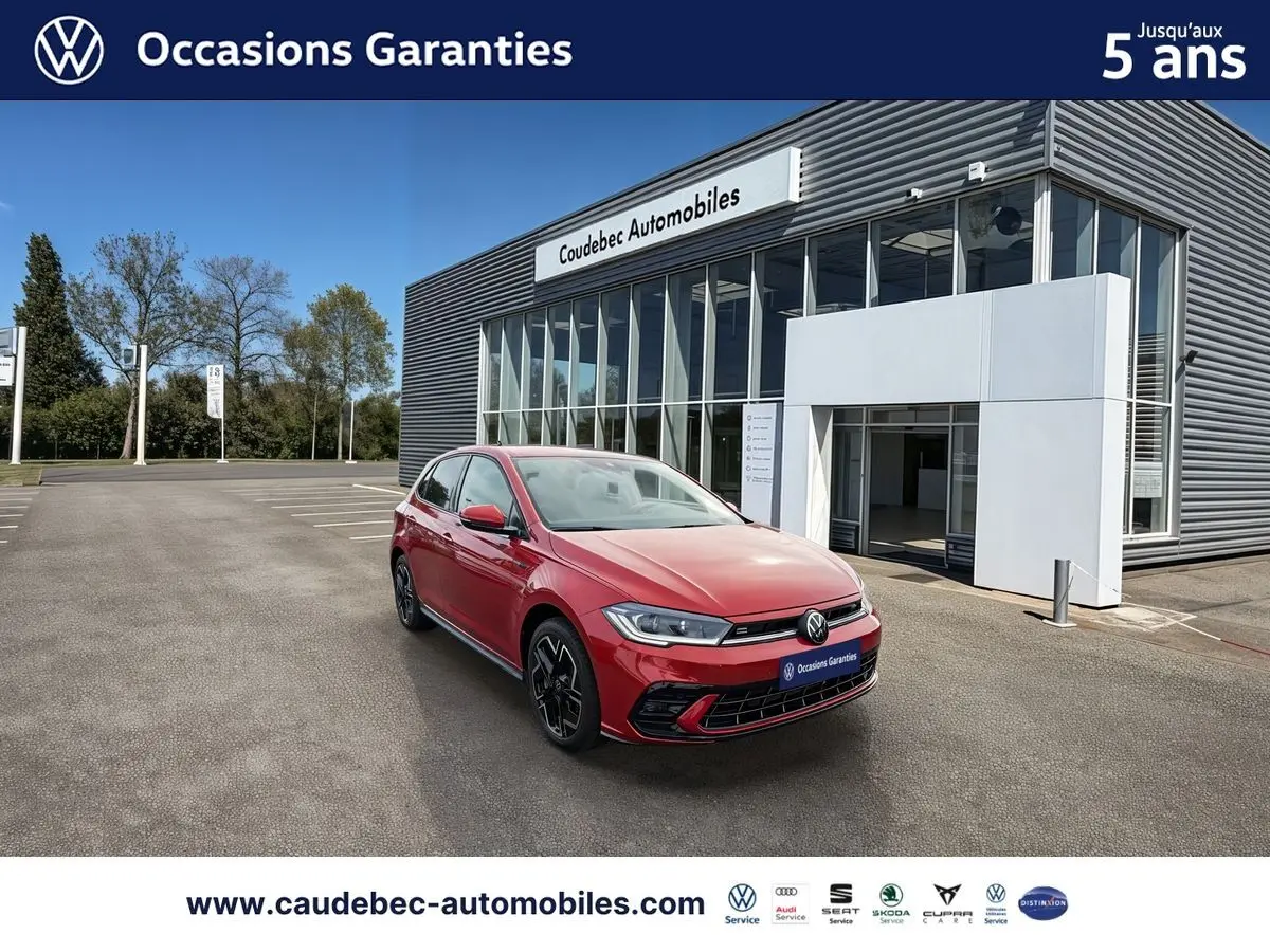 Volkswagen Polo rouge vue 3/4 avant droit, avec jantes alliage noires, stationnée devant un bâtiment moderne.
