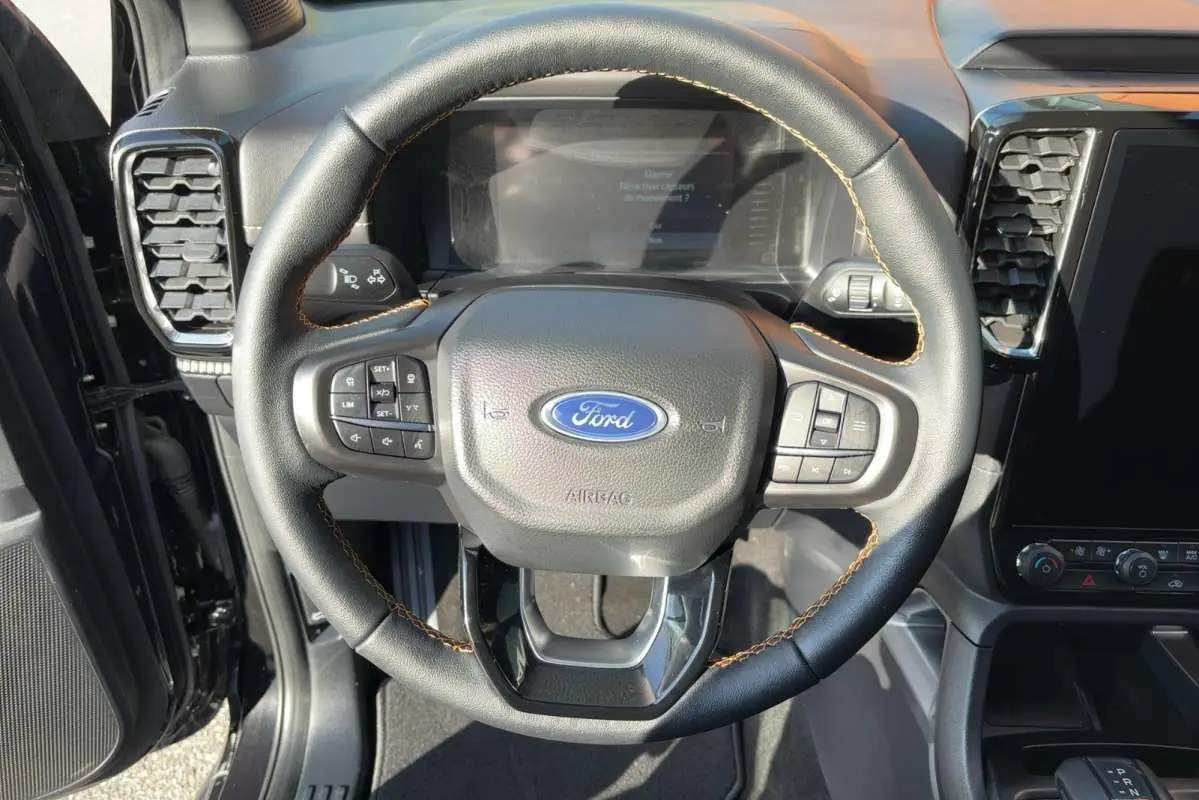 Vue rapprochée du volant cuir noir avec surpiqûres marron du Ford Ranger Wildtrak 2026, tableau de bord et écran tactile visibles.