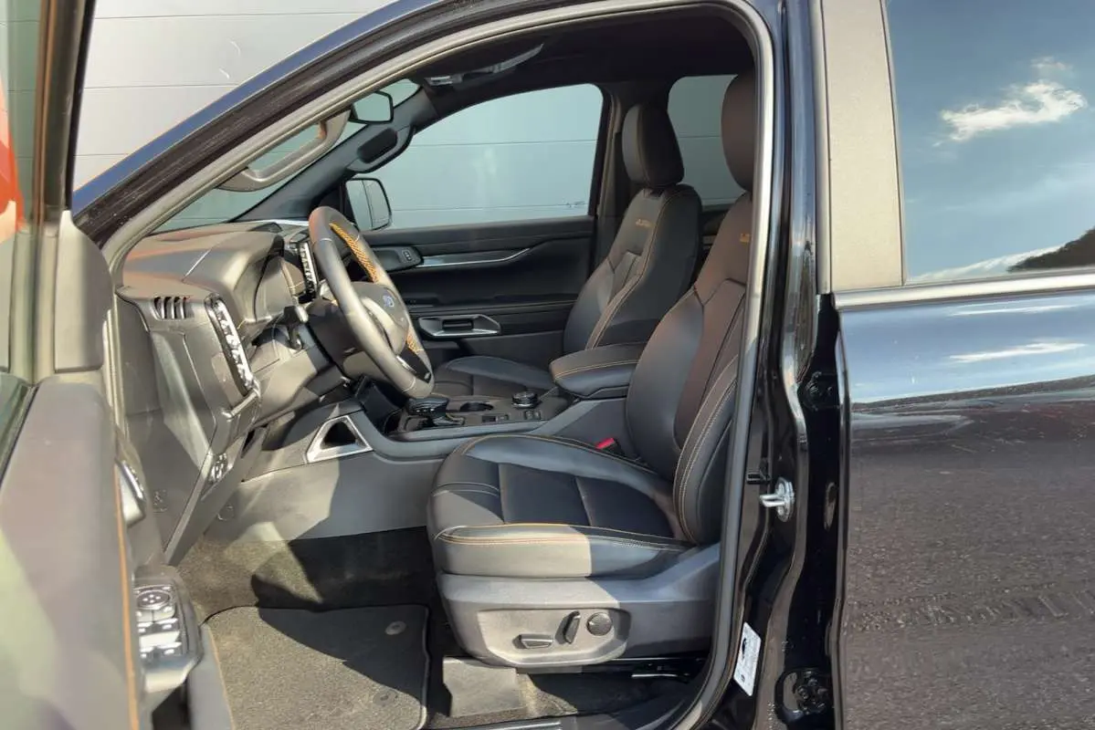 Vue intérieure côté conducteur du Ford Ranger noir agate, sièges en cuir avec surpiqûres orange et volant multifonctions.