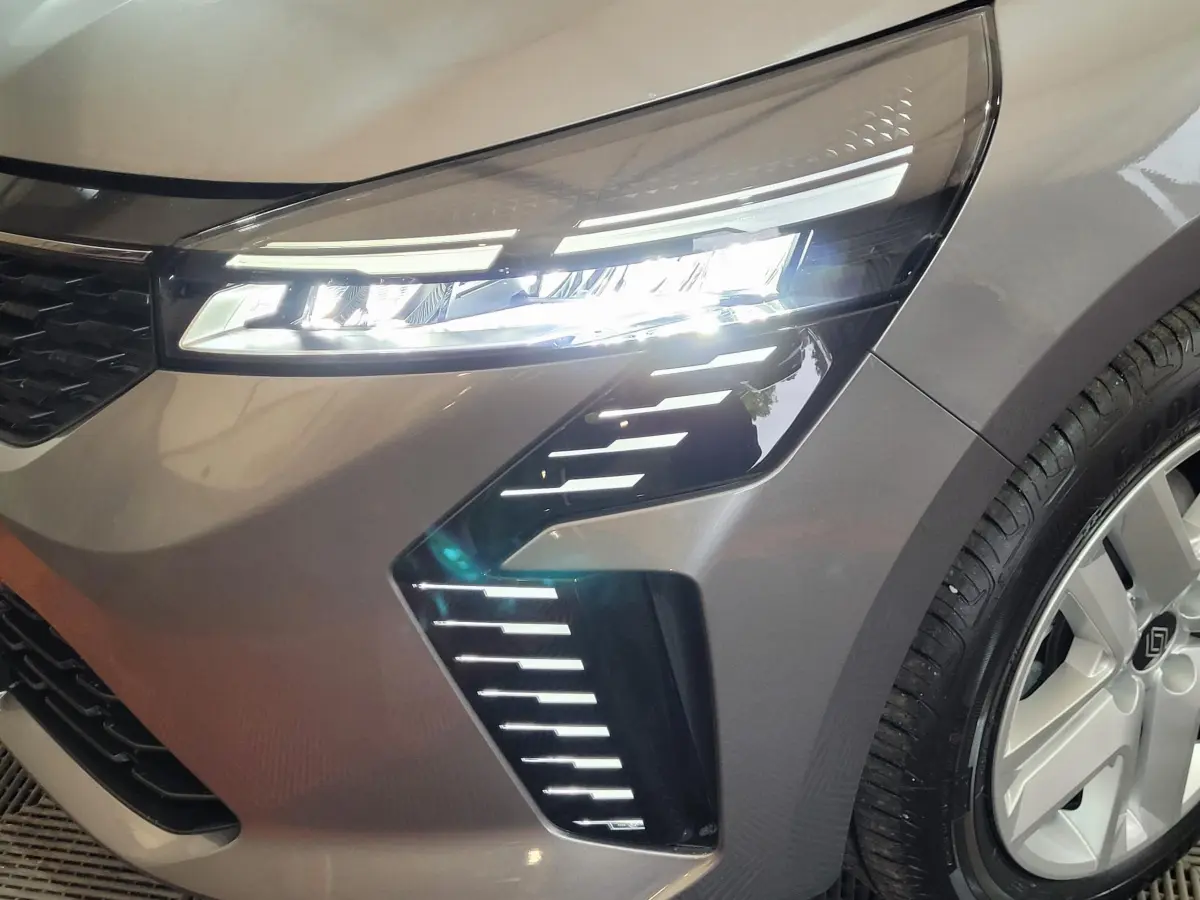 Gros plan sur le phare avant droit allumé d'une Renault Clio gris foncé avec jante alliage et calandre noire.