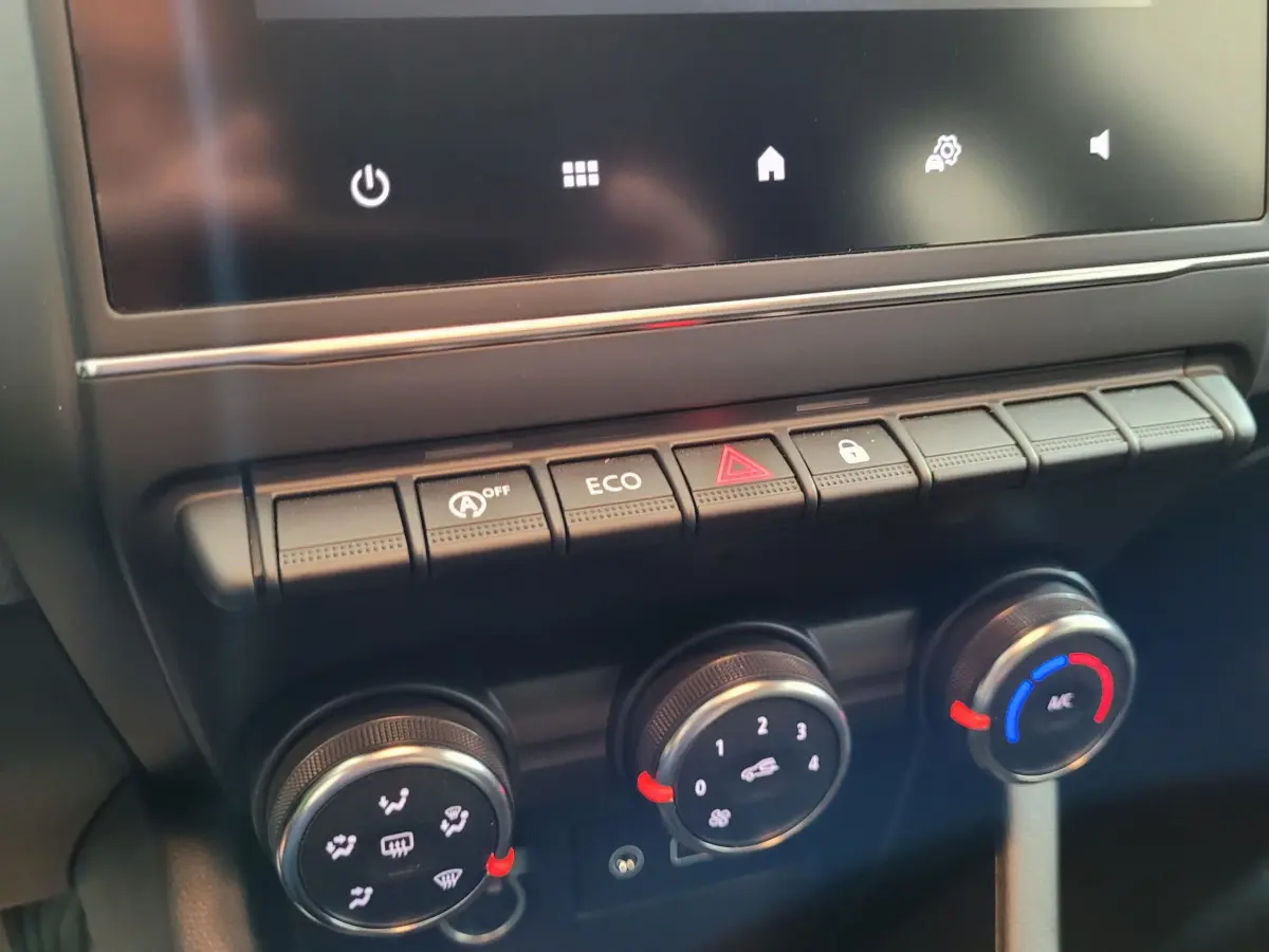 Gros plan sur la console centrale de la Renault Clio gris foncé, montrant les commandes de climatisation et les boutons fonctionnels.