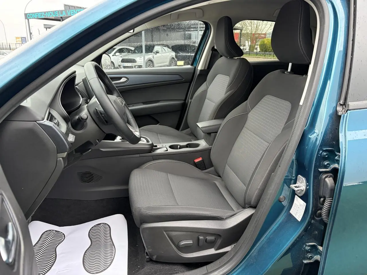 Vue intérieure côté conducteur de la Renault Arkana bleu Zanzibar, sièges tissu gris avec réglages électriques visibles.