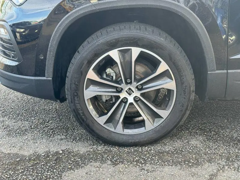 Gros plan sur la roue avant droite du SEAT Ateca noir métallique, mettant en valeur la jante alu au design moderne.