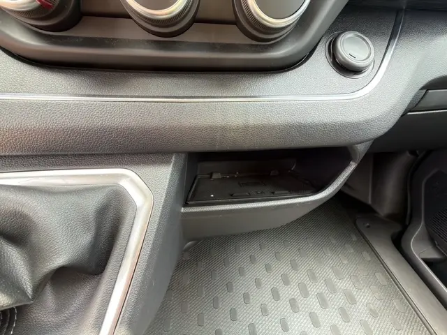Gros plan sur la console centrale noire du Nissan Primastar 2025, montrant la zone de recharge par induction et la commande circulaire.