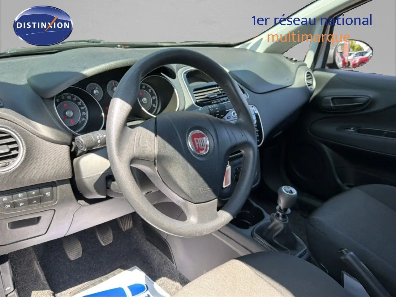 Vue intérieure côté conducteur de la Fiat Punto Street gris argent 2016, volant et levier de vitesse manuelle visibles.