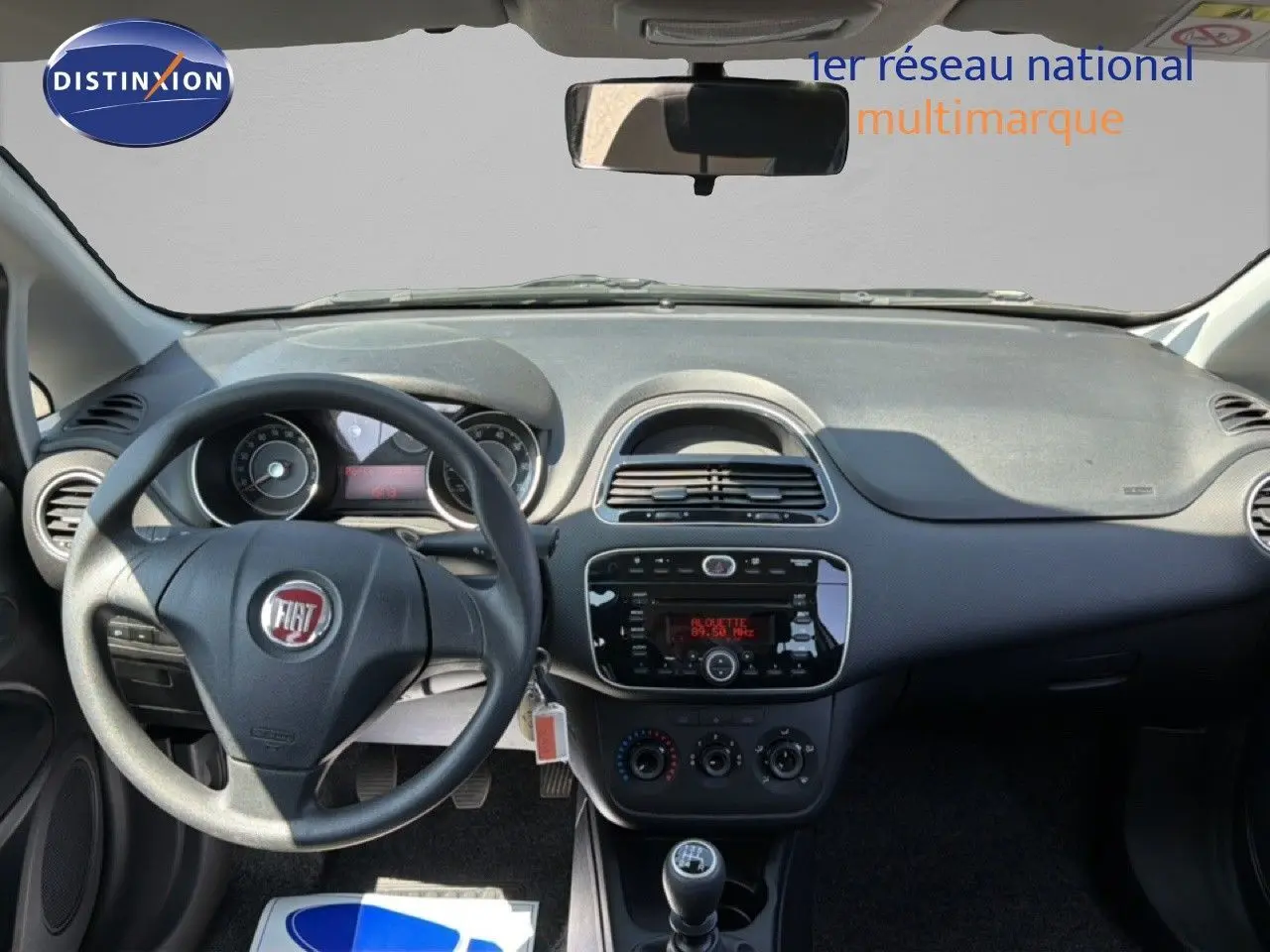 Vue intérieure frontale du tableau de bord gris foncé de la Fiat Punto Street 2016 avec volant, radio et levier de vitesse manuel.