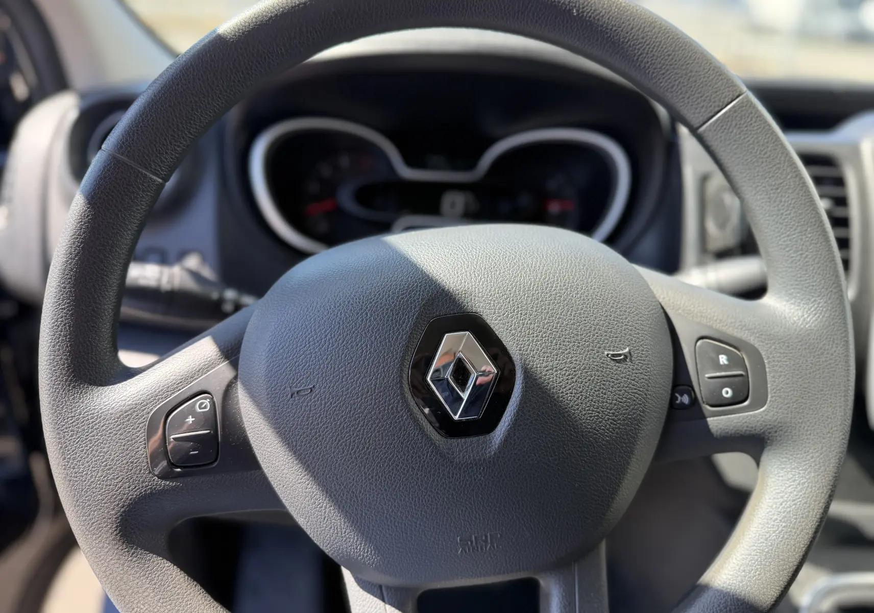 Gros plan sur le volant gris du Renault Trafic 2021 avec commandes intégrées et logo au centre.