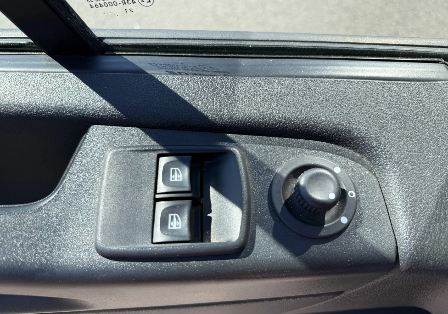Gros plan sur les commandes de lève-vitres et réglage des rétroviseurs côté conducteur d’un Renault Trafic gris.